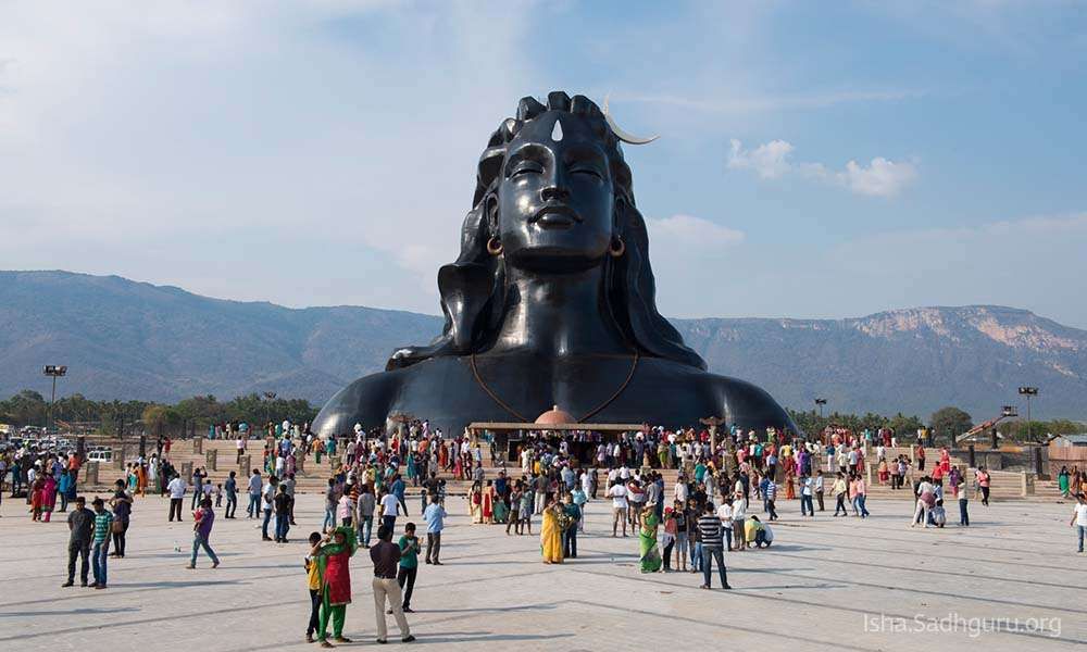 front of Adiyogi Shiva Statue and Yogeshwar temple with a crowd of visitors.